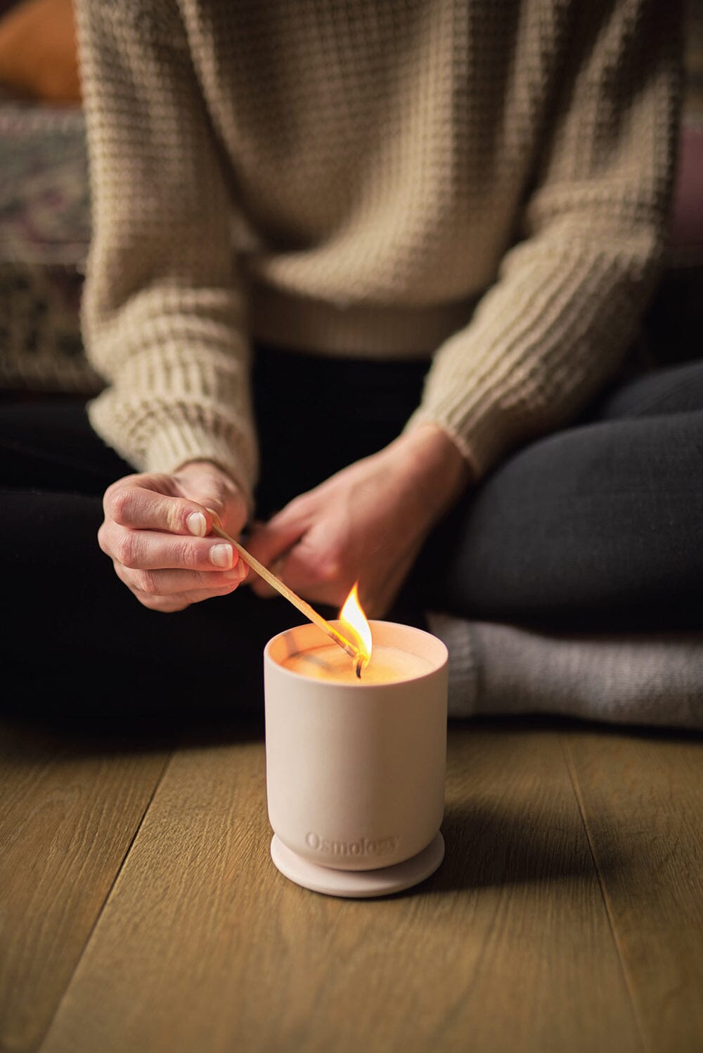 Osmology Himalayan Cedarleaf candle placed on the floor, being lit by match held by person sat cross legged on the floor